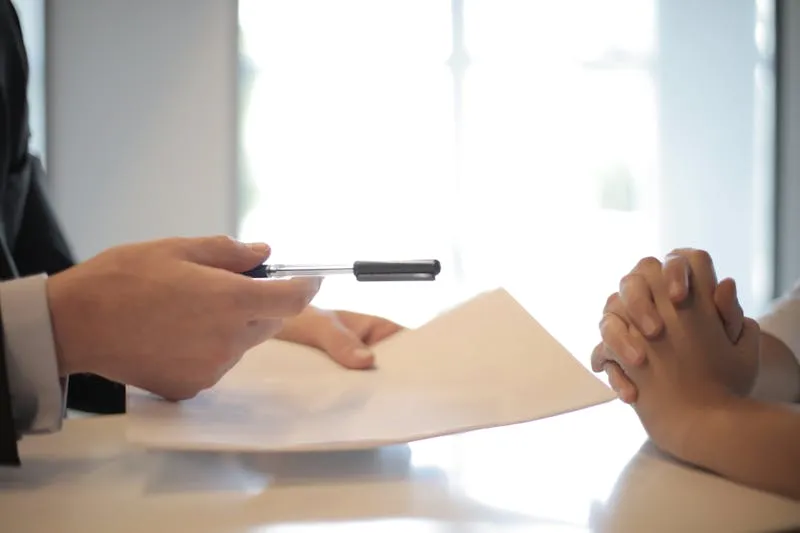 Person handing over a contract document across a desk