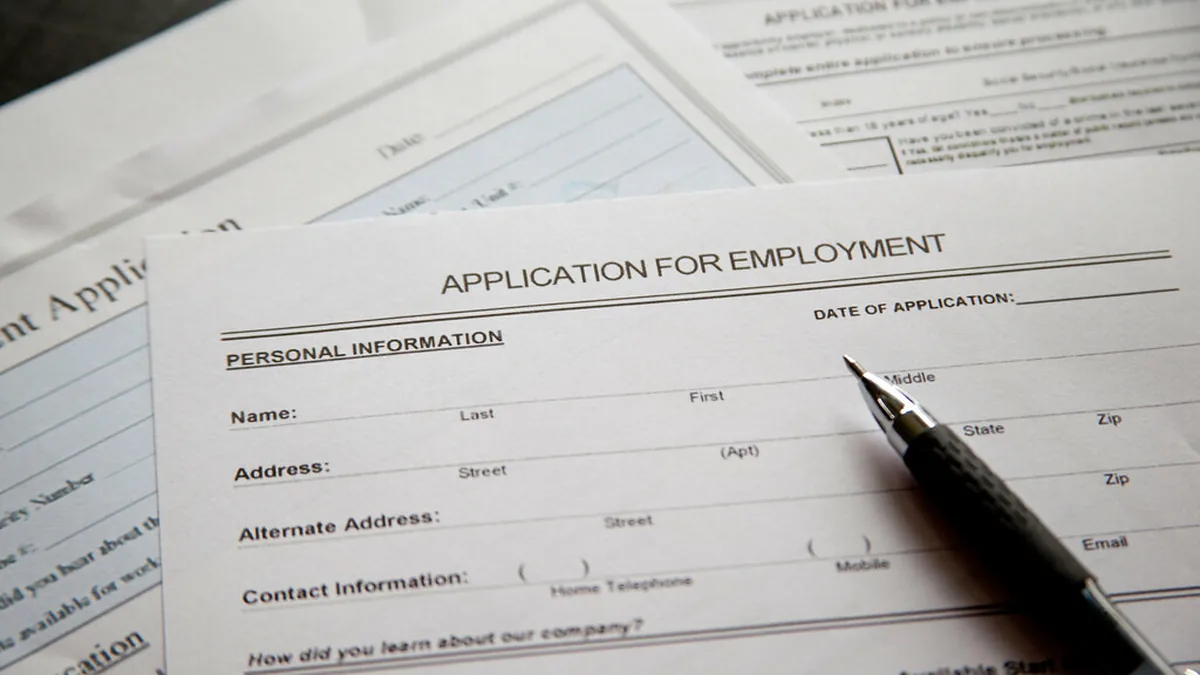 Employment application form with a pen — every new hire means paperwork, background checks, and compliance requirements