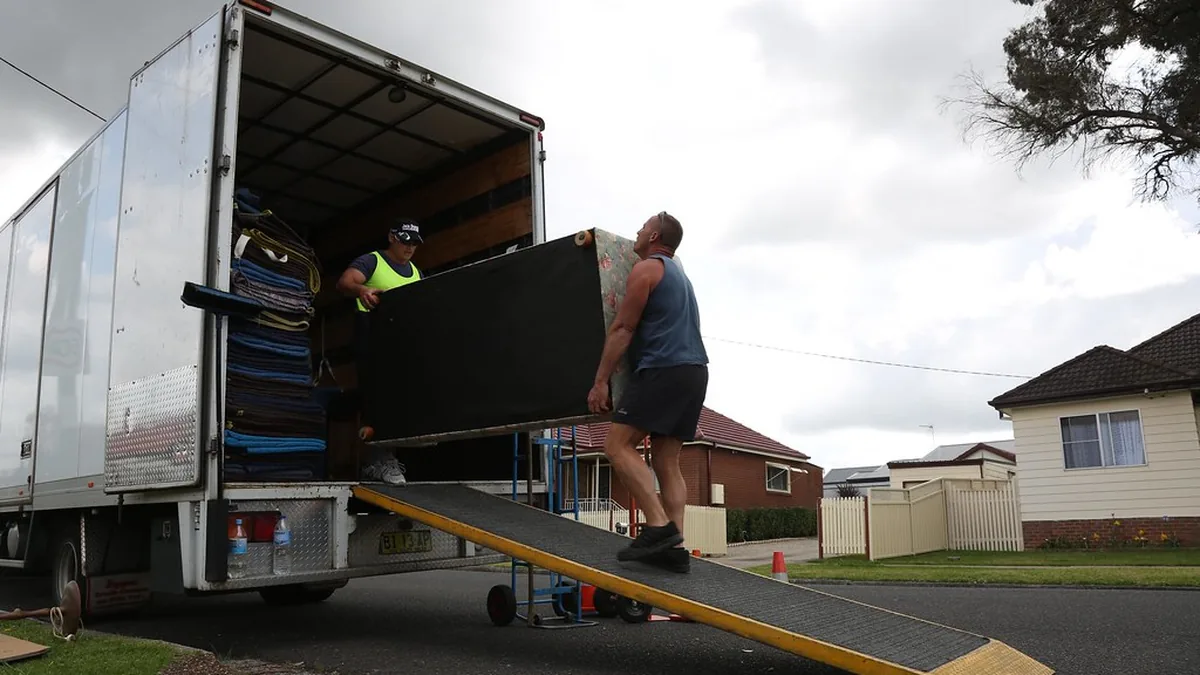 Two movers carrying furniture up a ramp into a moving truck — keeping good crews together through peak season is the real challenge