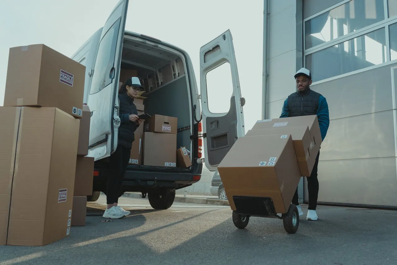 Two delivery workers unloading boxes from a van using a hand truck